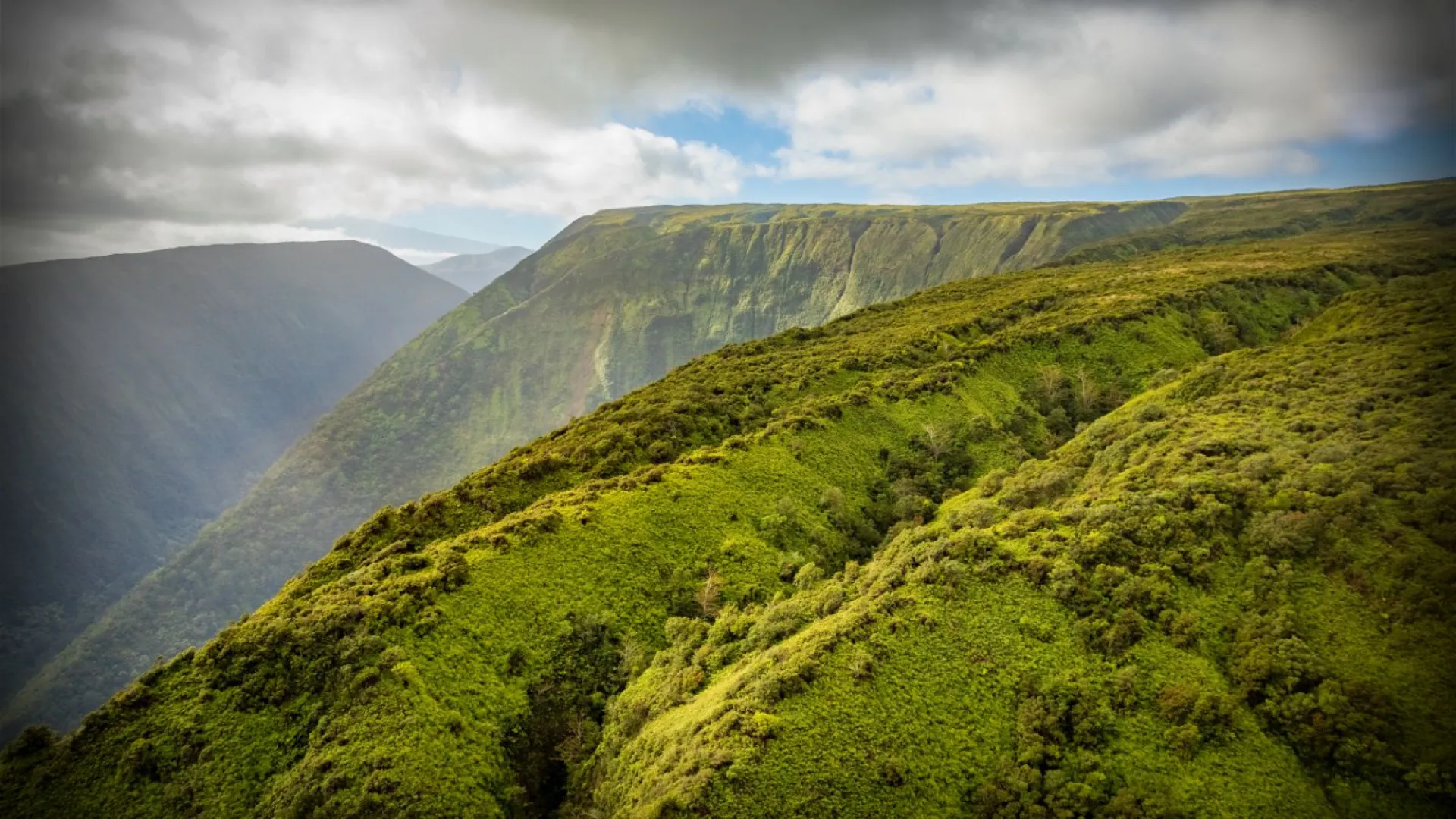 Lush green mountains under a cloudy sky.